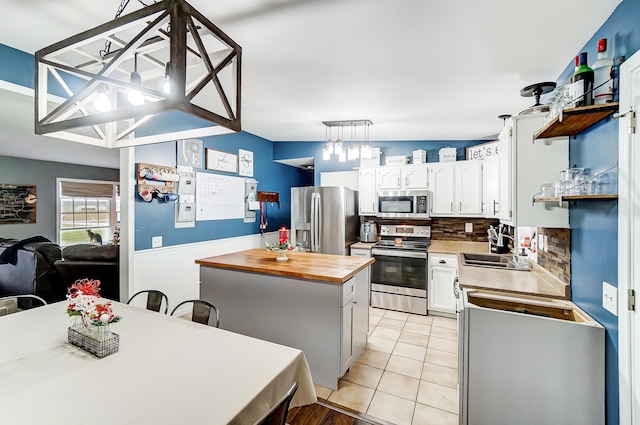 kitchen with appliances with stainless steel finishes, backsplash, a kitchen island, white cabinetry, and light tile patterned flooring