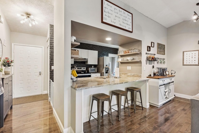 kitchen featuring appliances with stainless steel finishes, a breakfast bar, a textured ceiling, dark hardwood / wood-style floors, and white cabinetry