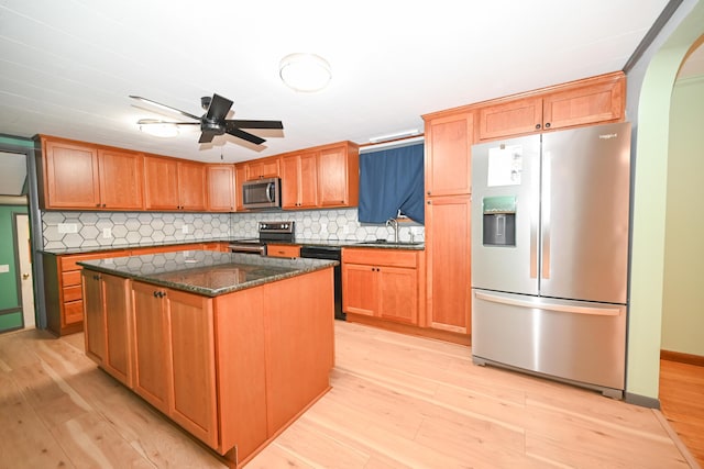 kitchen with tasteful backsplash, stainless steel appliances, a kitchen island, and light wood-type flooring