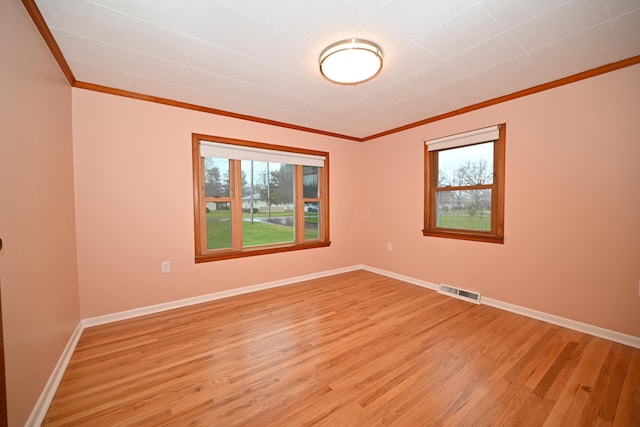 empty room featuring a healthy amount of sunlight, ornamental molding, and light hardwood / wood-style floors