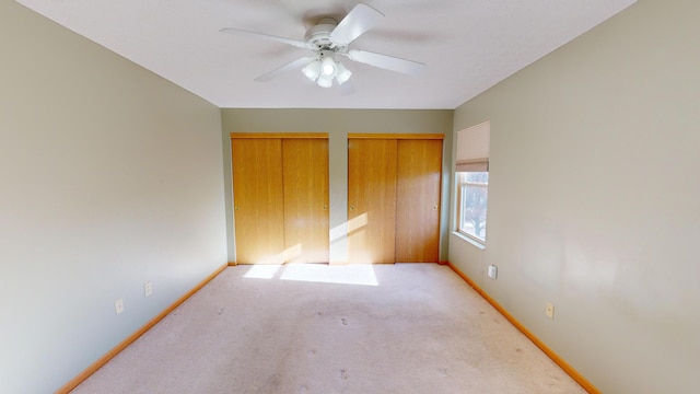 unfurnished bedroom featuring carpet flooring, ceiling fan, and multiple closets