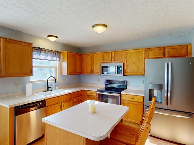 kitchen featuring a textured ceiling, stainless steel appliances, a kitchen island, and sink