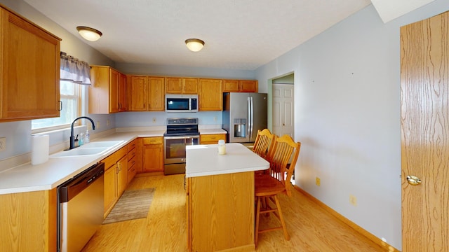 kitchen with sink, a kitchen island, light wood-type flooring, and appliances with stainless steel finishes