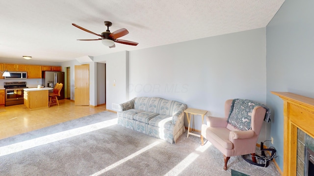 living area with a tile fireplace, ceiling fan, and a textured ceiling