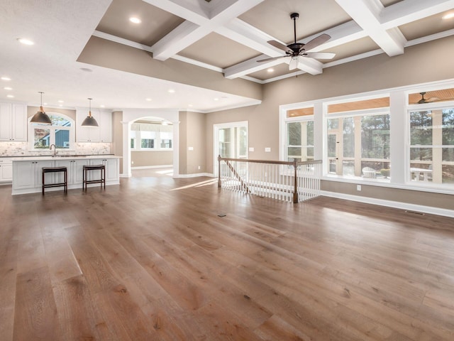 unfurnished living room featuring coffered ceiling, ceiling fan, hardwood / wood-style flooring, beam ceiling, and sink