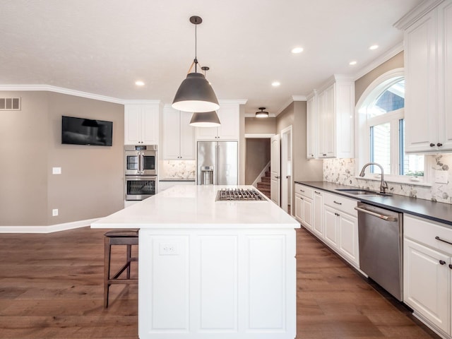 kitchen with appliances with stainless steel finishes, pendant lighting, a kitchen island, white cabinets, and sink