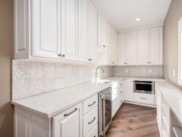 kitchen featuring stainless steel oven, white cabinets, beverage cooler, and sink