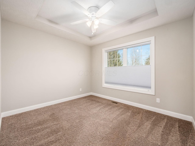 empty room with ceiling fan, carpet, and a tray ceiling