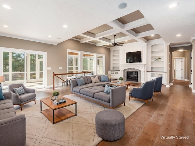 living room with beam ceiling, a fireplace, built in features, ceiling fan, and coffered ceiling