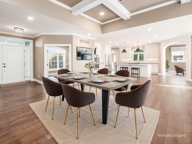 dining space with light wood-type flooring, ornamental molding, beamed ceiling, and sink