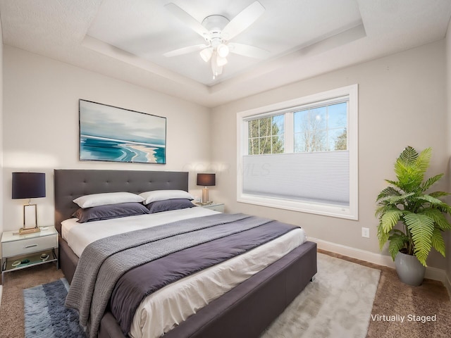 carpeted bedroom with ceiling fan and a raised ceiling