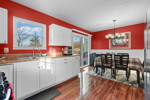 kitchen featuring a textured ceiling, dark wood-type flooring, decorative light fixtures, a notable chandelier, and white cabinets