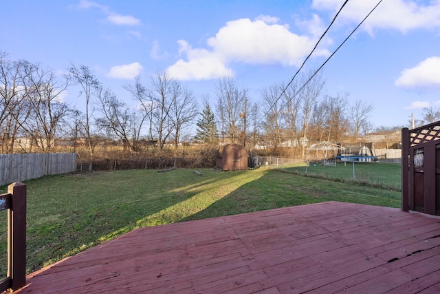 wooden terrace featuring a lawn, a storage shed, and a trampoline