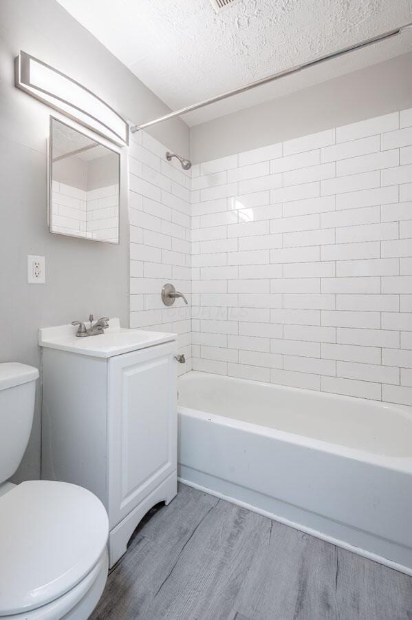 full bathroom featuring toilet, tiled shower / bath, vanity, hardwood / wood-style flooring, and a textured ceiling