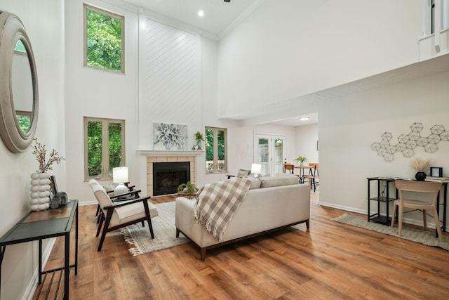 living room with french doors, crown molding, a tile fireplace, hardwood / wood-style flooring, and a high ceiling