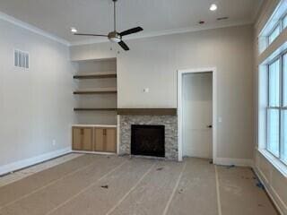 unfurnished living room with baseboards, a fireplace, visible vents, and crown molding