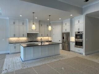 kitchen with a center island with sink, crown molding, dark countertops, appliances with stainless steel finishes, and white cabinetry