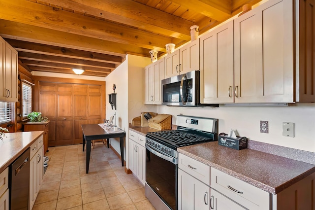 kitchen with light tile patterned floors, appliances with stainless steel finishes, dark countertops, and beam ceiling