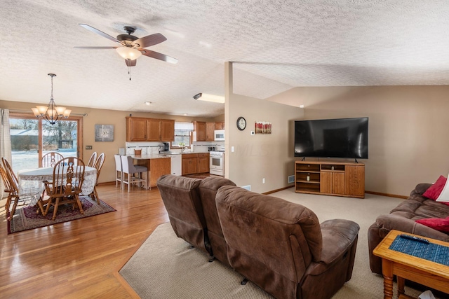 living room featuring ceiling fan with notable chandelier, light hardwood / wood-style floors, a textured ceiling, and lofted ceiling