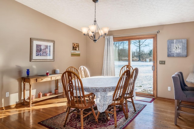 dining room featuring hardwood / wood-style floors, a textured ceiling, a notable chandelier, and lofted ceiling