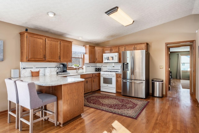 kitchen featuring kitchen peninsula, vaulted ceiling, backsplash, white appliances, and light hardwood / wood-style floors