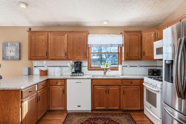 kitchen with white appliances, a textured ceiling, sink, light wood-type flooring, and kitchen peninsula