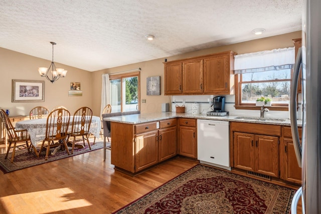 kitchen featuring white dishwasher, sink, kitchen peninsula, pendant lighting, and light stone counters