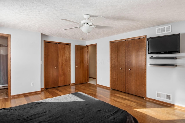 unfurnished bedroom featuring ceiling fan, two closets, a textured ceiling, and hardwood / wood-style flooring