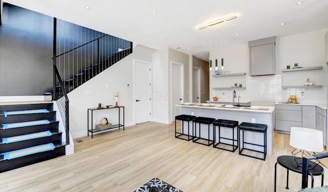 kitchen with a kitchen bar, gray cabinets, decorative backsplash, and light hardwood / wood-style flooring