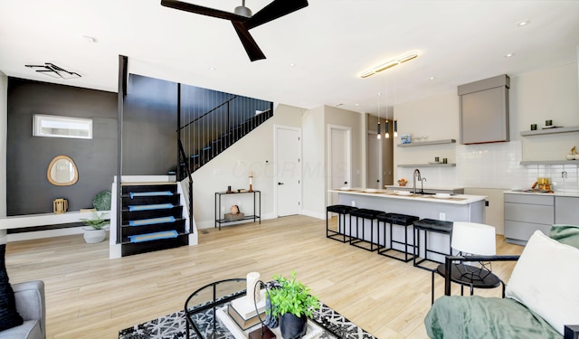 living room featuring ceiling fan, sink, and light hardwood / wood-style flooring