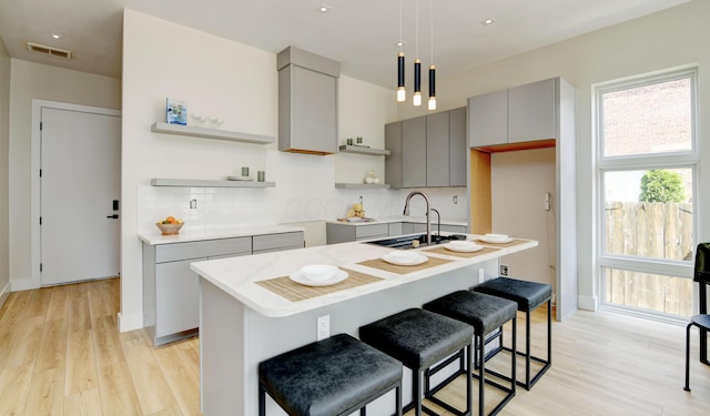 kitchen with gray cabinets, a center island with sink, backsplash, and a kitchen bar