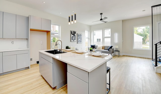 kitchen with gray cabinets, decorative light fixtures, sink, a kitchen island with sink, and light hardwood / wood-style floors