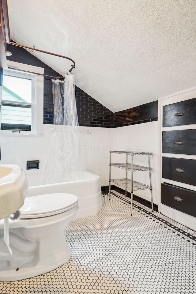 bathroom featuring a textured ceiling, tile walls, tile patterned floors, and lofted ceiling