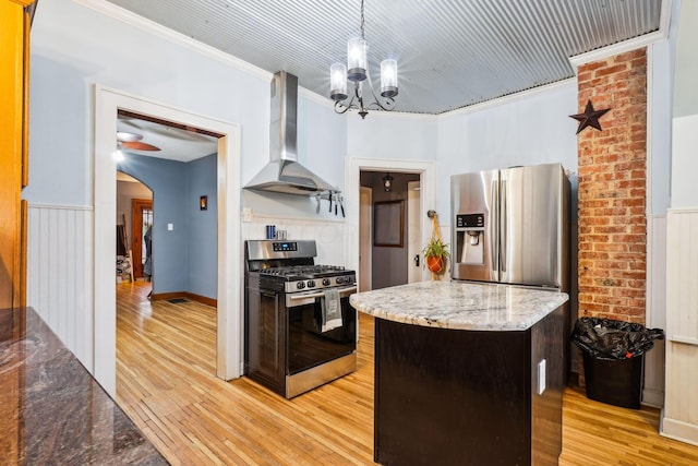 kitchen featuring wall chimney exhaust hood, hanging light fixtures, stainless steel appliances, light hardwood / wood-style flooring, and crown molding