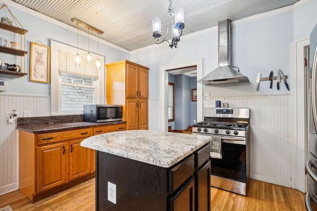 kitchen featuring appliances with stainless steel finishes, light wood-type flooring, wall chimney range hood, decorative light fixtures, and a center island