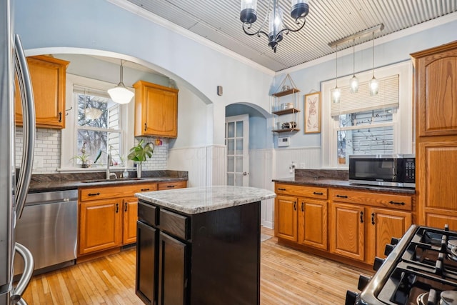 kitchen featuring crown molding, sink, light wood-type flooring, appliances with stainless steel finishes, and decorative light fixtures