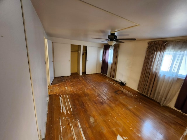 unfurnished bedroom with ceiling fan, wood-type flooring, and two closets