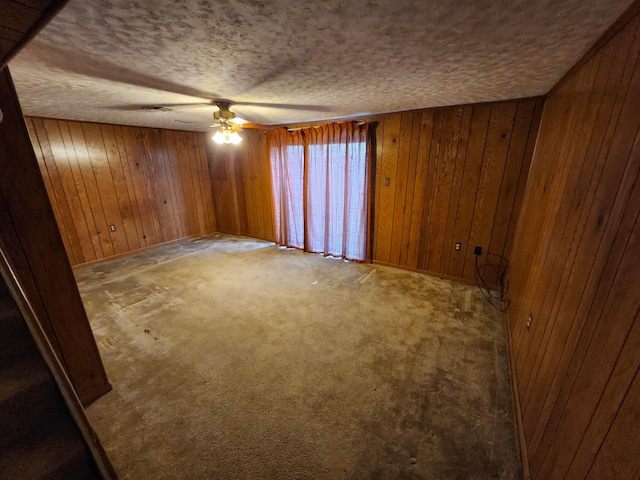 unfurnished room featuring ceiling fan, a textured ceiling, and wooden walls