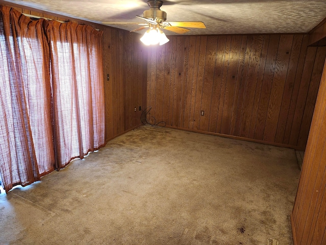 carpeted spare room with a textured ceiling, ceiling fan, and wooden walls