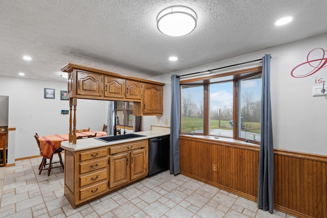 kitchen with kitchen peninsula, a textured ceiling, wooden walls, sink, and black dishwasher