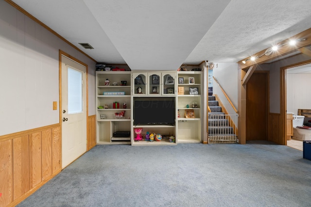 carpeted living room featuring wood walls, ornamental molding, and a textured ceiling