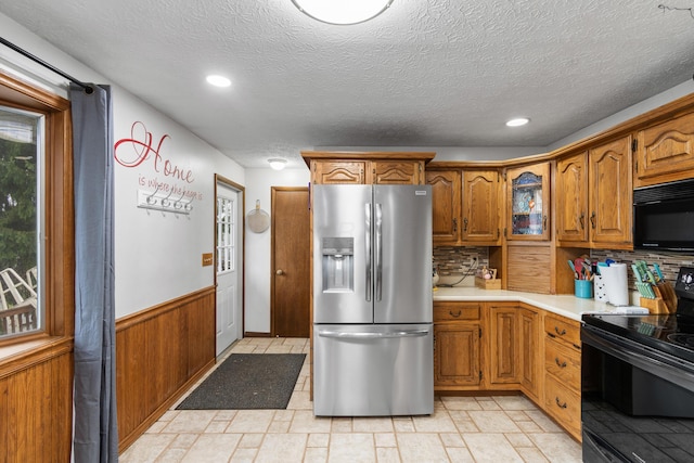 kitchen with a textured ceiling, tasteful backsplash, wood walls, and black appliances