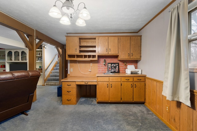 kitchen with wood walls, dark carpet, ornamental molding, a textured ceiling, and decorative light fixtures