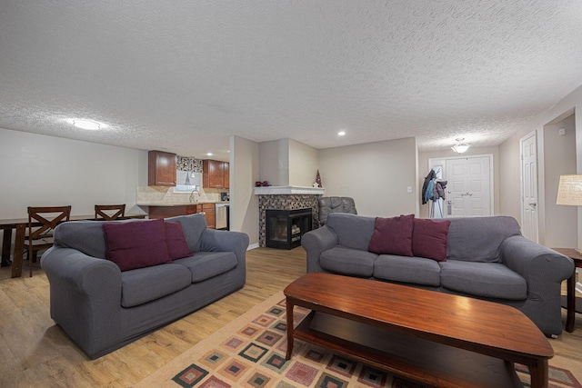 living room featuring a tiled fireplace, sink, a textured ceiling, and light wood-type flooring