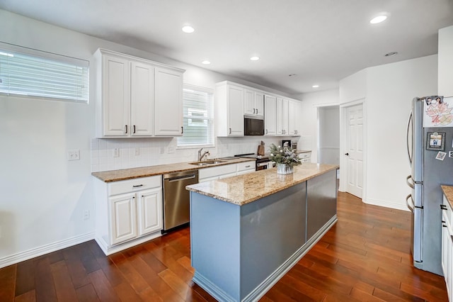 kitchen with sink, white cabinets, light stone counters, a kitchen island, and appliances with stainless steel finishes