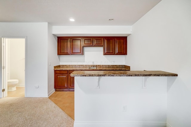 kitchen with a kitchen bar, kitchen peninsula, light carpet, and sink