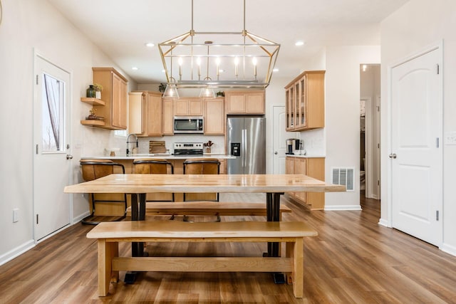 kitchen with light brown cabinetry, decorative backsplash, pendant lighting, and stainless steel appliances