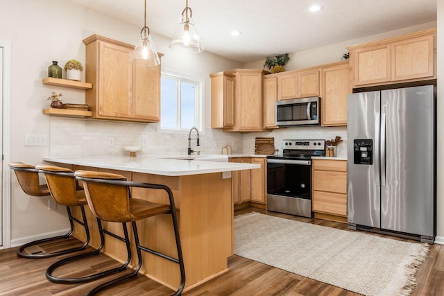 kitchen featuring a kitchen breakfast bar, sink, hanging light fixtures, hardwood / wood-style flooring, and stainless steel appliances