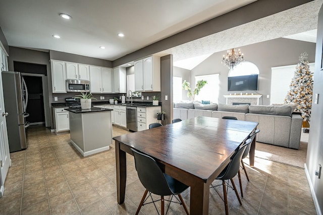 kitchen with lofted ceiling, sink, white cabinetry, stainless steel appliances, and a chandelier