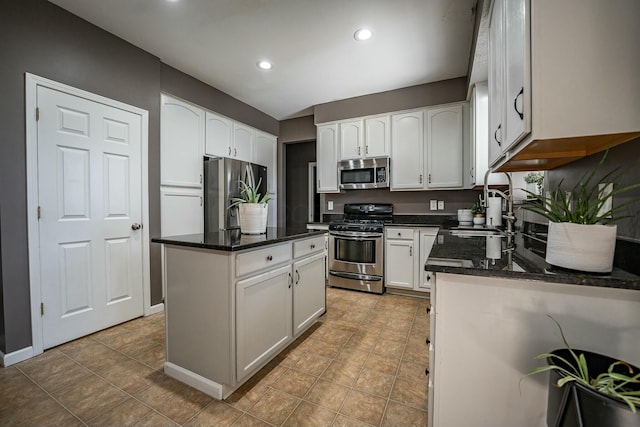 kitchen with white cabinets, sink, dark stone countertops, appliances with stainless steel finishes, and a kitchen island